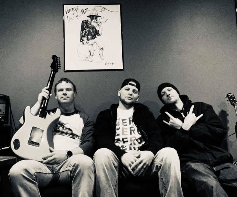The three band members sitting on a couch, black and white