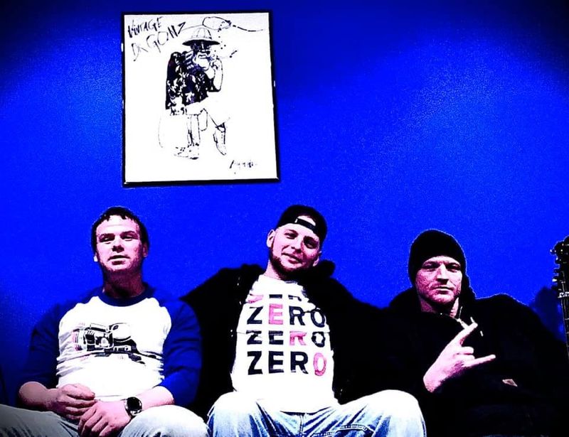 The three band members sitting against a blue wall